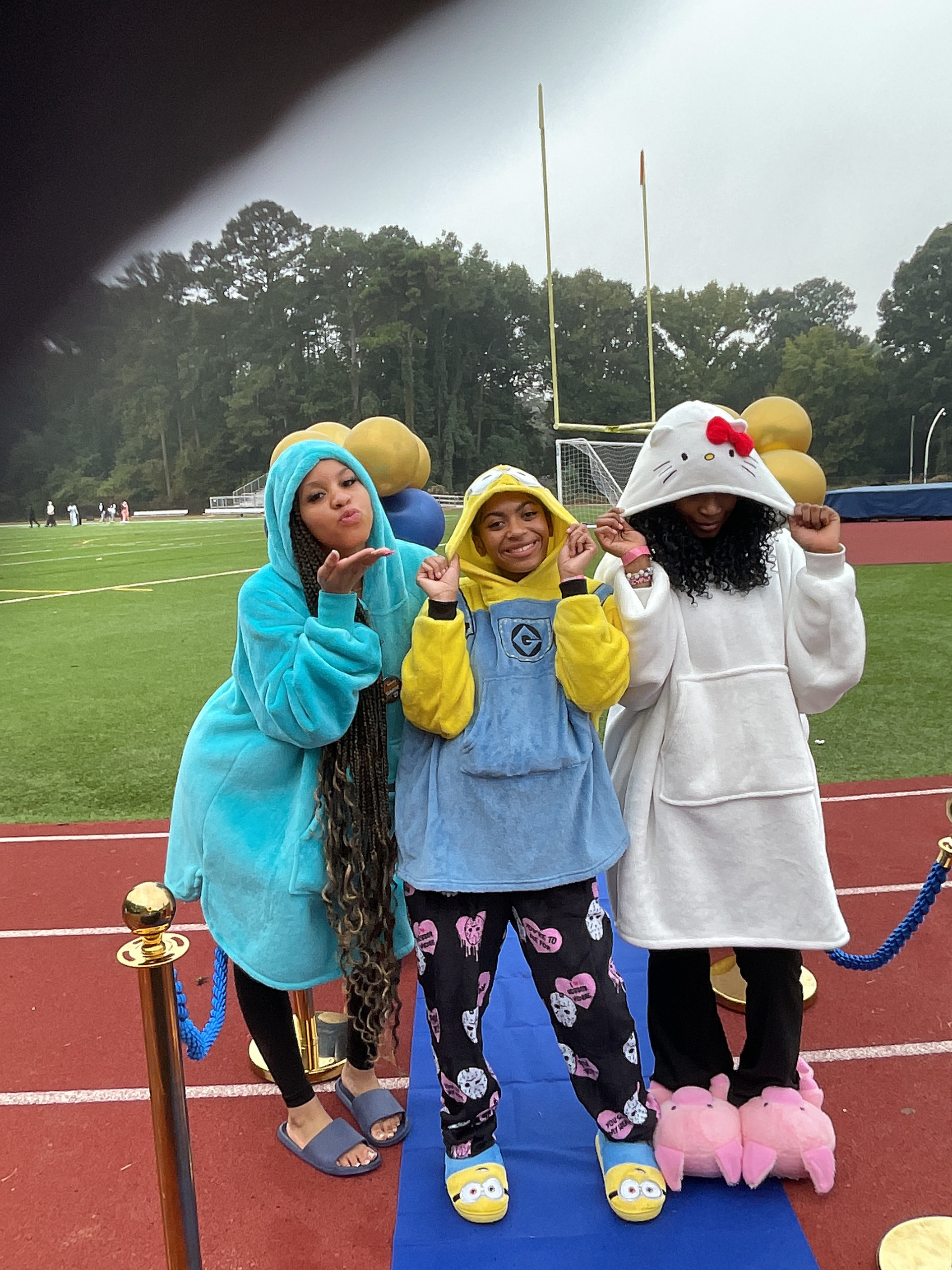 Three friends in fleece character onesies posing on the blue mat on the track at sunrise