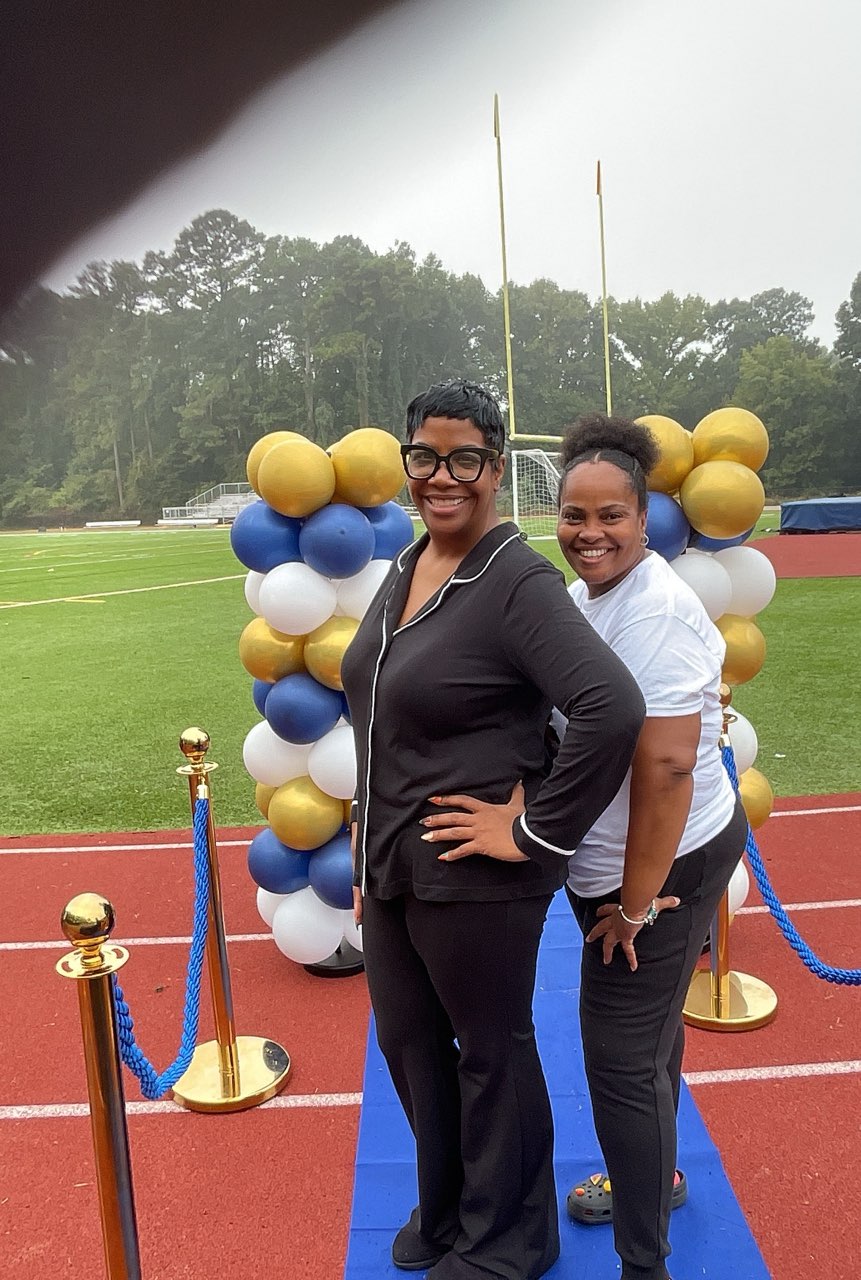 Two smiling women in front of the balloon arch on the blue mat