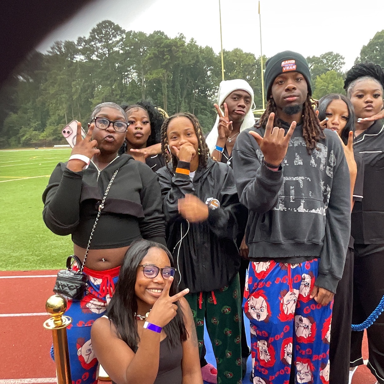 A group of eight posing with hand signs on the red track at senior sunrise